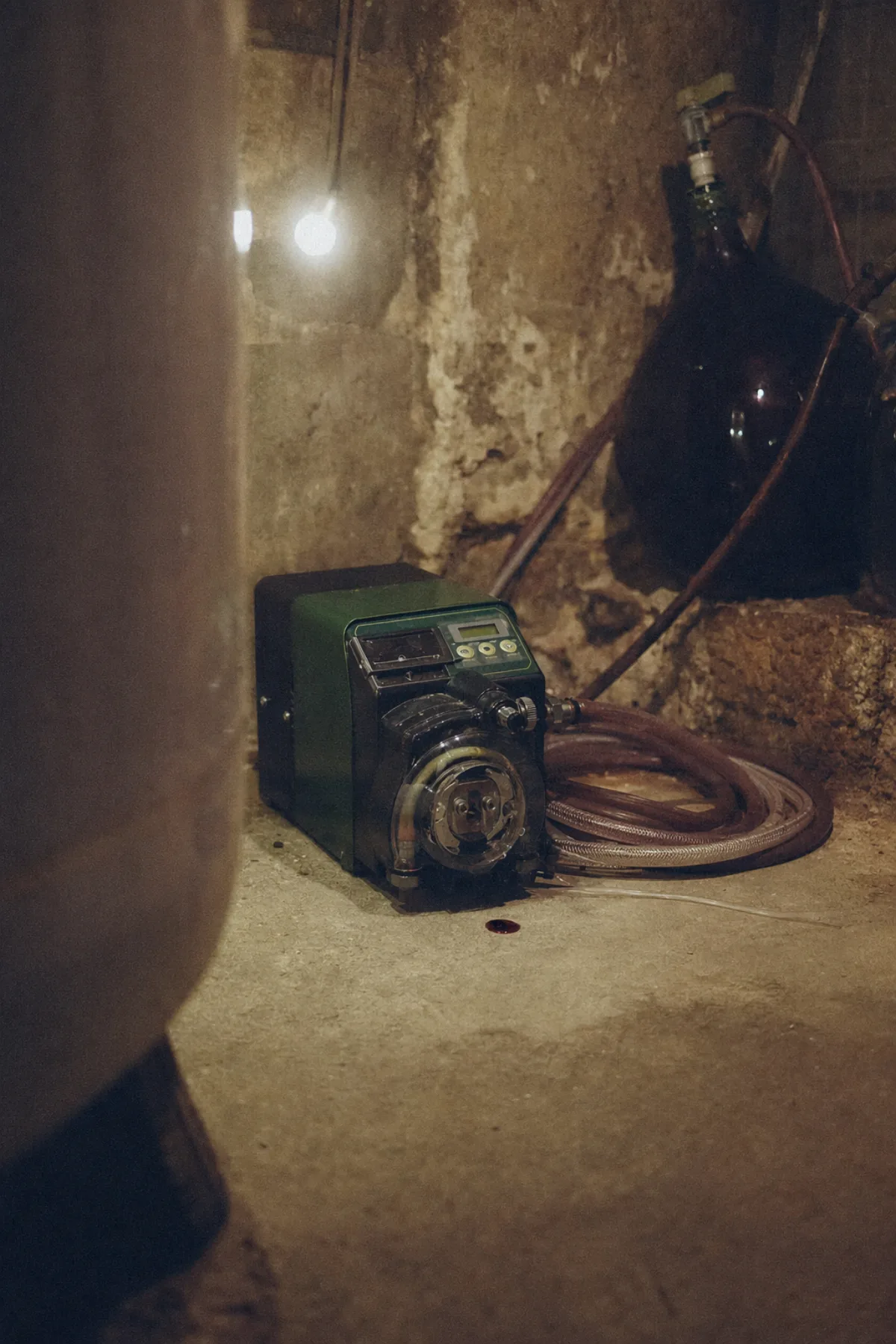 A dark green peristaltic pump on a concrete cellar floor