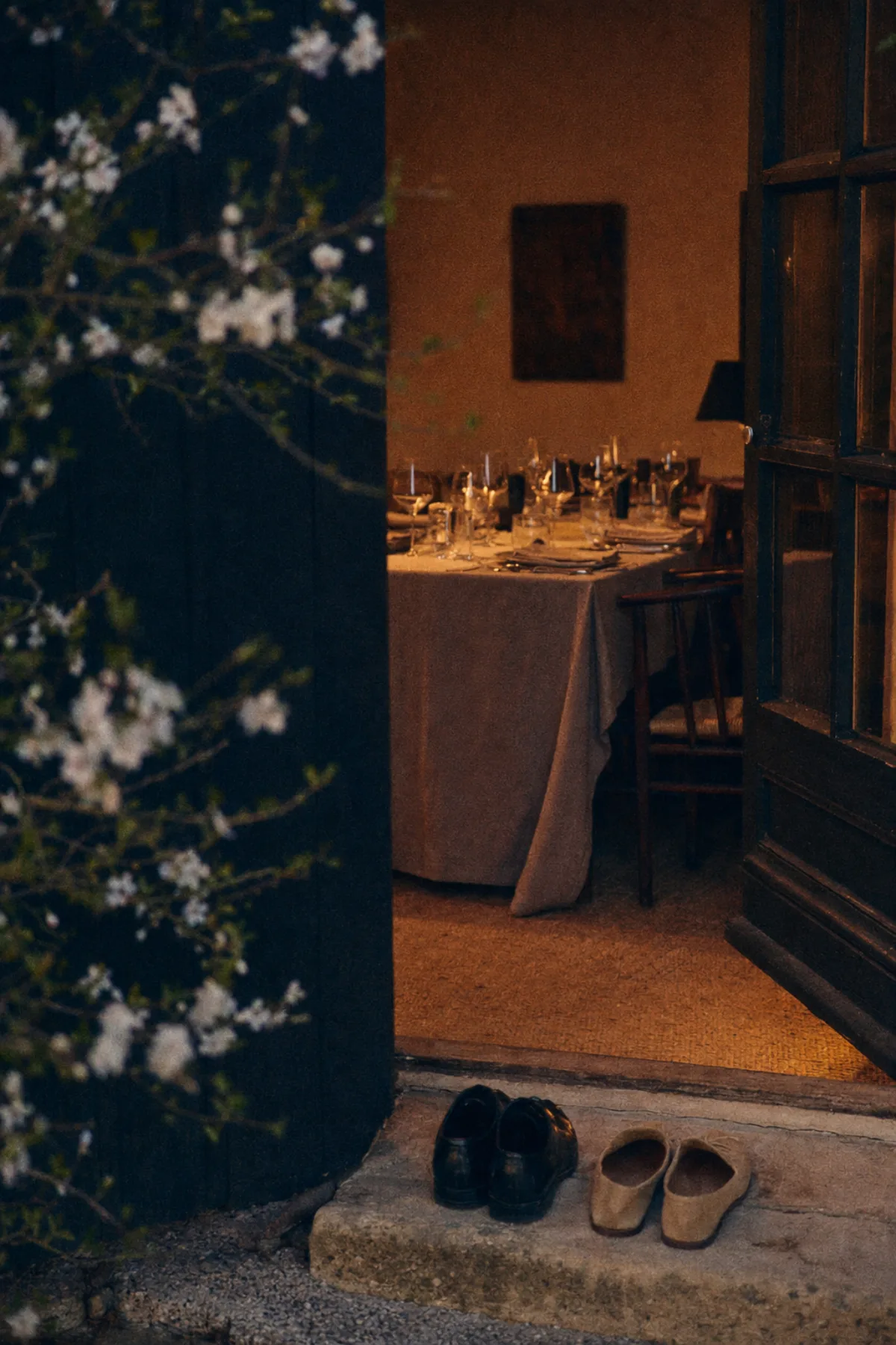 The open door of the maison at dusk, warm amber light inside